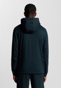 Felpa con cappuccio verde scuro, in tessuto elasticizzato, design minimalista, siluette aderente, cuciture piatte, maniche lunghe, senza loghi o motivi visibili.