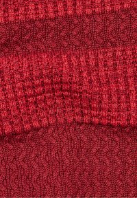 Tessuto lavorato a maglia rosso con un motivo testurizzato. Presenta sezioni alternate di punti lisci e a coste, creando un aspetto a strati.