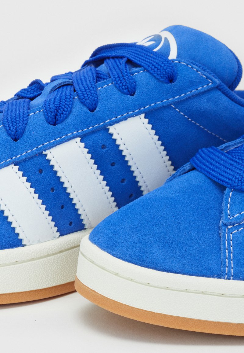 Blaue Wildledersneaker mit weißen Streifenakzenten, Stoffsenkeln, Gummisohlen und kreisförmigen Belüftungsöffnungen.