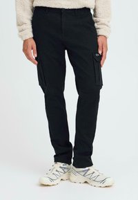 Schwarze Cargo-Hosen aus Baumwolle mit Seitentaschen und slim fit Design. Tragen mit weißen Sneakern und einem grauem strukturierten Pullover.