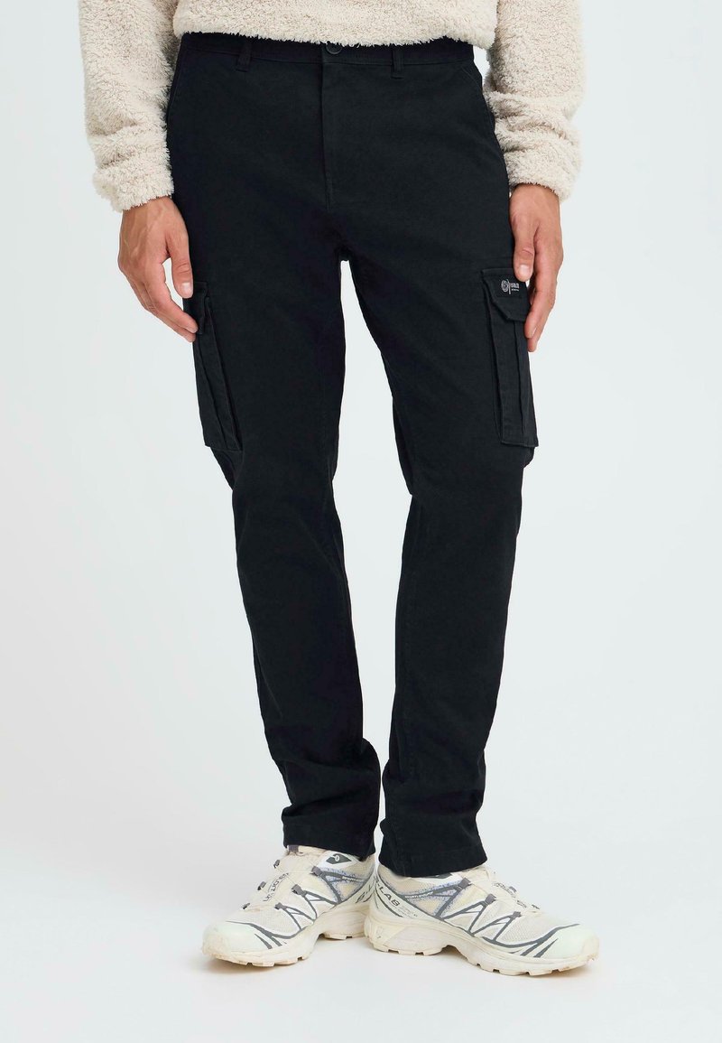 Schwarze Cargo-Hosen aus Baumwolle mit Seitentaschen und slim fit Design. Tragen mit weißen Sneakern und einem grauem strukturierten Pullover.