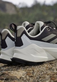 Paire de chaussures de randonnée Adidas Terrex noires et blanches posées sur un terrain rocheux à l'extérieur.