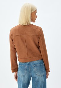 Bruine suède jas met een getailleerd silhouet, lange mouwen en een cropped lengte, gecombineerd met lichtblauwe denim jeans.