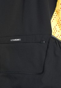 Giacca atletica nera con logo "ULTRAWEAVES", tasca con zip e accenti gialli a motivo sulle maniche. Texture liscia.