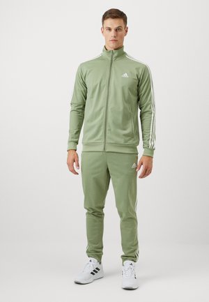 Grønt træningssæt i glat stof, med en lynlåstrøje med høj krave, hvide detaljer og tre striber på ærmer og bukser.