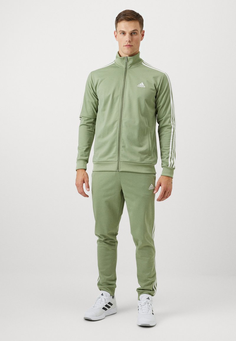 Zeleni trenirka od glatke tkanine, s jaknom na patent zatvarač sa visokim ovratnikom, bijelim detaljima i tri pruge na rukavima i hlačama.