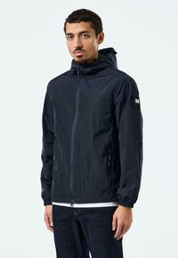 Marineblau leichte Jacke mit Kapuze, Reißverschluss, elastischen Bündchen und Seitentaschen. Strukturiertes Material mit dezentem Glanz.
