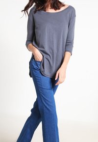 Grå långärmad tröja med vid halsringning och sidofickor, ihopparad med blå raka jeans med en enkel design och slät textur.