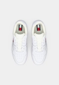 Baskets en cuir blanc avec une texture lisse. Présentent une pointe perforée, un design à lacets, et des accents rouges et bleus avec logo sur la languette.