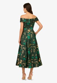 Zelené květinové šaty s volným výstřihem. Mají zlaté akcenty a rozšířenou sukni. Nosené s béžovými vysokými podpatky.
