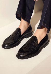 Zwarte leren instappers met een krokodillenstructuur, met een slip-on ontwerp en decoratieve horizontale strepen op de bovenkant. Lage hak.