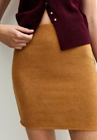 Falda amarilla mostaza con canalé y silueta ajustada, combinada con una blusa de punto burdeos que presenta botones dorados en el escote.
