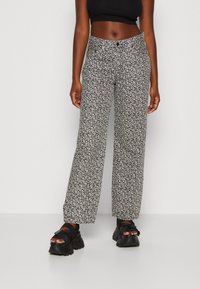 Pantalones de pierna ancha con patrón floral en blanco y negro, de cintura alta, con cierre de botón y textura de tela suave. Combinados con sandalias negras de suela gruesa.