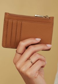 Brown textured leather wallet with multiple card slots and a zippered pocket, held in a hand against a neutral background.