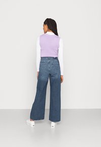 Top sem mangas em lã lilás, combinado com calças de ganga azul de perna larga. As calças têm uma cintura alta e uma textura suave. Ténis brancos complementam o visual.