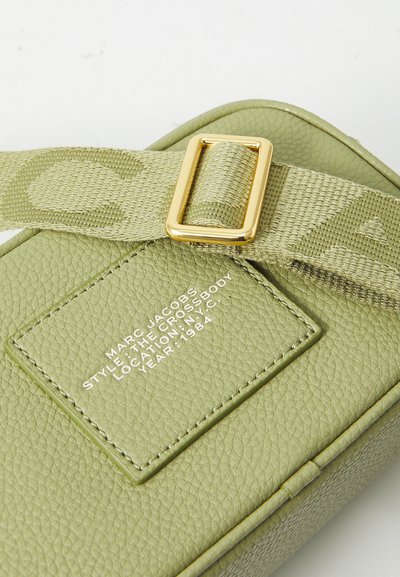 Světle zelená kožená crossbody taška s texturovaným povrchem, zlatými kovovými doplňky a vzorovaným textilním popruhem s detaily značky.