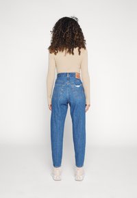 Jeans en denim bleu taille haute avec une coupe décontractée, dotés d'une étiquette en cuir classique, de poches arrière et de détails déchirés.