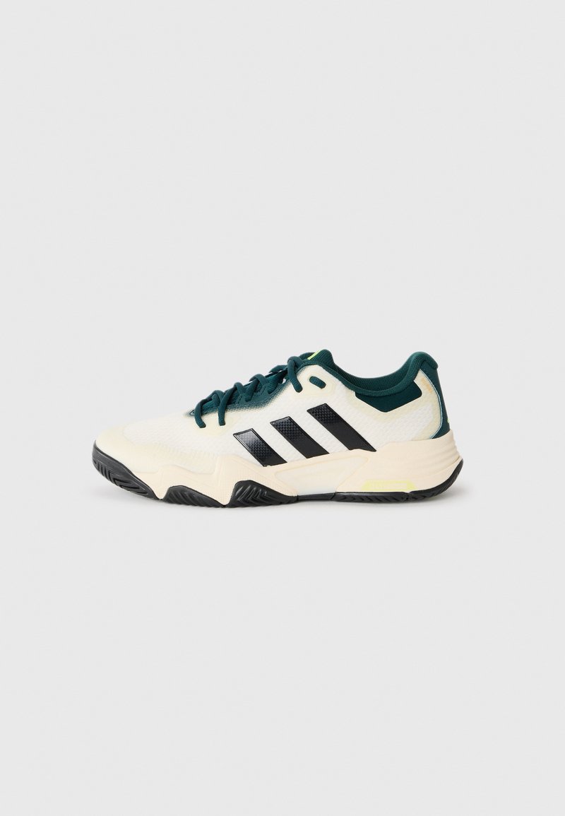 White and dark green athletic sneaker with black stripes, textured sole, and lace-up front on plain light gray background.