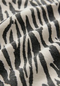 Gros plan d’un tissu froissé avec des rayures noires irrégulières de zèbre sur fond blanc.