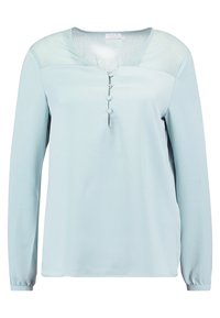 Blouse à manches longues bleu clair en tissu lisse. Encolure en V avec trois boutons décoratifs à l'avant. Panneau transparent aux épaules.