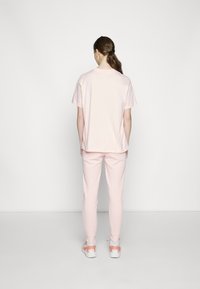 Růžové bavlněné tričko s krátkými rukávy, doplněné o odpovídající růžové tepláky. Hladký povrch; volný střih bez viditelných vzorů nebo akcentů.