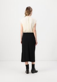 Beige topp med flytende fasong og frynsete kanter, detalj med nøkkelhull i ryggen, kombinert med et midilengdes svart skjørt. svarte hæle ankelstøvler med ribbet detaljer.