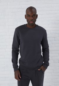 Dunkelgrauer Sweatshirt mit Rundhalsausschnitt und langen Ärmeln, das eine glatte Textur sowie gerippte Bündchen und Saum aufweist, getragen mit passender Hose.