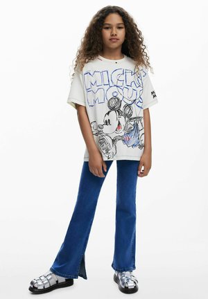 Camiseta blanca de gran tamaño con un gráfico colorido de Mickey Mouse, combinada con vaqueros acampanados azules y sandalias de plataforma plateadas con tiras.