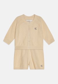 Cardigan bej tricotat și set scurt cu margini încrețite, guler rotund, nasturi frontal și logo brodat pe cardigan.