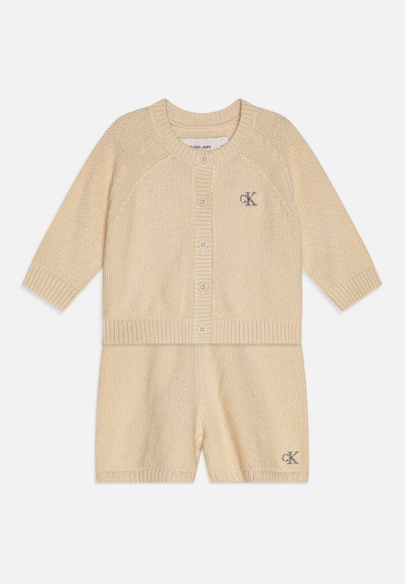 Cardigan bej tricotat și set scurt cu margini încrețite, guler rotund, nasturi frontal și logo brodat pe cardigan.