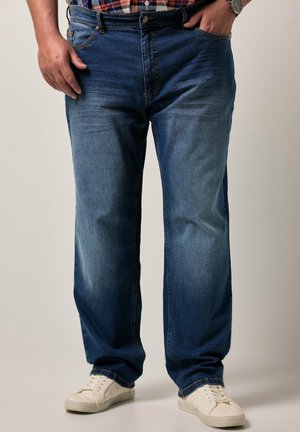 Jeans de denim azul con un corte recto, lavado desgastado y costuras en contraste. Combinados con zapatillas blancas, exhibidos sobre un fondo neutro.