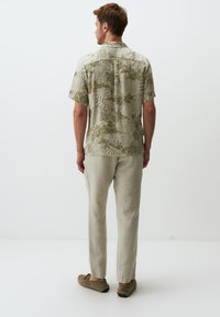 Korte mouwen, lichtbeige shirt met groen bloemenpatroon, gecombineerd met lichte linnen broek en bruine instappers. Achteraanzicht.