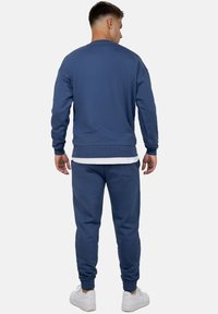 Felpa blu e pantaloni coordinati, realizzati in tessuto morbido. Presentano polsini a coste, vestibilità comoda e una tasca sul retro dei pantaloni.