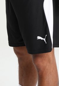 Pantalones cortos deportivos negros con paneles laterales blancos y un logo blanco de Puma en el muslo izquierdo, fabricados con un material suave y ligero.