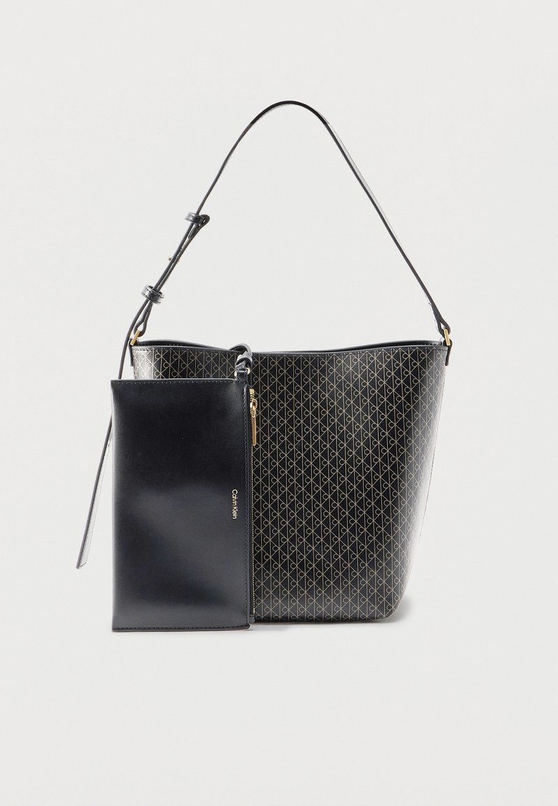Μαύρη τσάντα Calvin Klein με χρυσό λογότυπο, γεωμετρικό μοτίβο, ρυθμιζόμενο ιμάντα ώμου και προσαρτημένη μαύρη λείο θήκη με φερμουάρ.