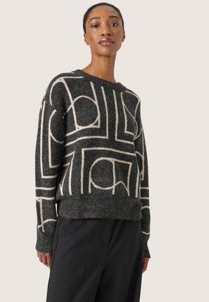 Gebreide trui met een zwarte basis en contrasterende witte geometrische patronen. Heeft een relaxte pasvorm en ribbelzoom en manchetten.