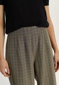Gray plaid trousers with pleats, featuring a pattern of thin black and orange lines, paired with a black short-sleeve top.