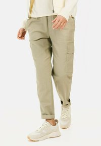 Lys beige cargo bukser med en afslappet pasform, som har sidelommer og manchetter, kombineret med hvide og beige sneakers.