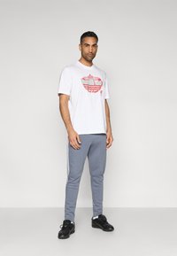 Valge T-särk punase graafilise mustriga, hallide dressipükstega, mille külgedel on valged triibud, ning mustade tossudega.