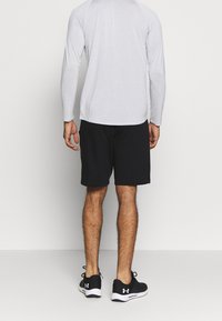 Schwarze Shorts mit einem elastischen Bund und einem schlichten Design, kombiniert mit einem hellgrauen Langarmshirt, getragen mit schwarzen Sportschuhen.