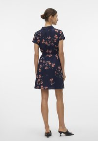 Vestido floral azul marinho com mangas curtas, cintura ajustada e saia ampla. Apresenta um tecido suave e um delicado padrão de flores cor-de-rosa.