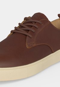 Chaussure décontractée en cuir marron avec lacets assortis et panneaux cousus, associée à une semelle en caoutchouc beige clair.