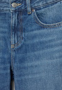 Close-up of blue denim jeans front with metal button, belt loop, and stitched pocket details.