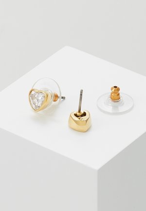 Gold heart-shaped stud earrings with clear stone centers and transparent disc backs on a white surface.