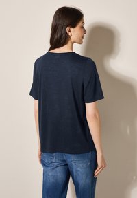Camiseta de manga corta azul marino con cuello redondo y corte relajado. Textura suave con un ligero brillo, el dobladillo termina a la altura de la cadera.