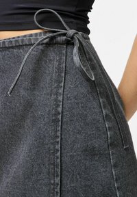 Pilkas džinsinis sijonas su surišamu juosmeniu, subtilia tekstūra ir tiesia pjūvio dizainu, turintis šoninio siūlės detalę.