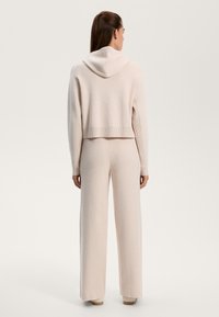 Felpa corta a maglia di un rosa chiaro, con cappuccio e orlo a coste, abbinata a pantaloni a gamba larga. Tessuto morbido con una vestibilità rilassata.