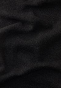 Tessuto nero con una superficie morbida e testurizzata, caratterizzato da sottili variazioni di luce e ombra, che creano un aspetto drappeggiato.