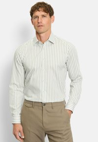 Hellgrünes und weiß gestreiftes Langarmshirt mit spitzem Kragen und Knopfleiste, kombiniert mit braunen Hosen. Hat kontrastierende Manschetten.