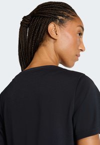 Maglietta nera a maniche corte con scollo rotondo, caratterizzata da una texture liscia e dettagli di cuciture sottili. Capelli acconciati a trecce.